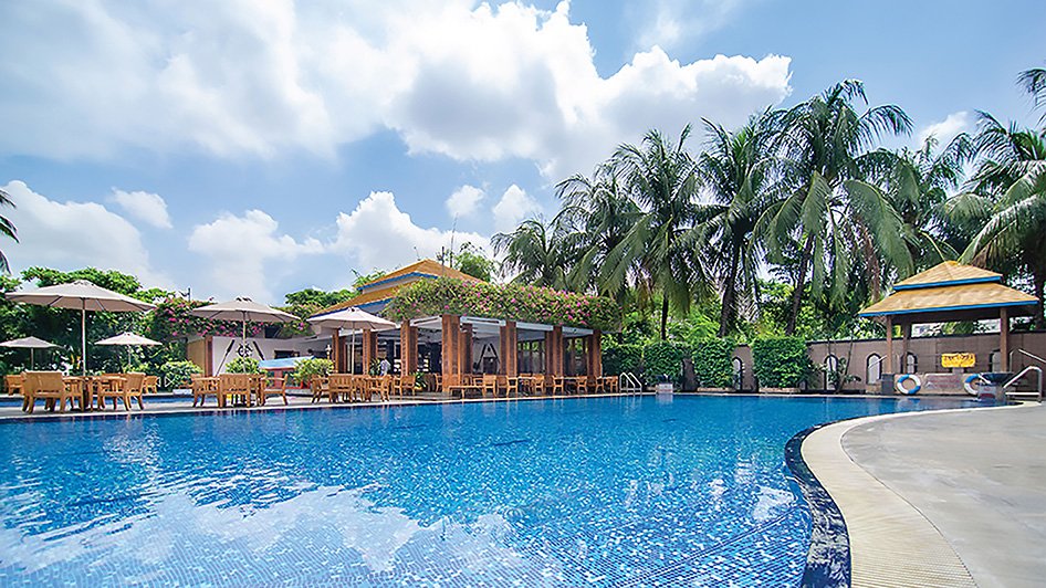 Outdoor swimming pool with poolside cafe and palm trees at Pan Pacific Sonargaon Dhaka