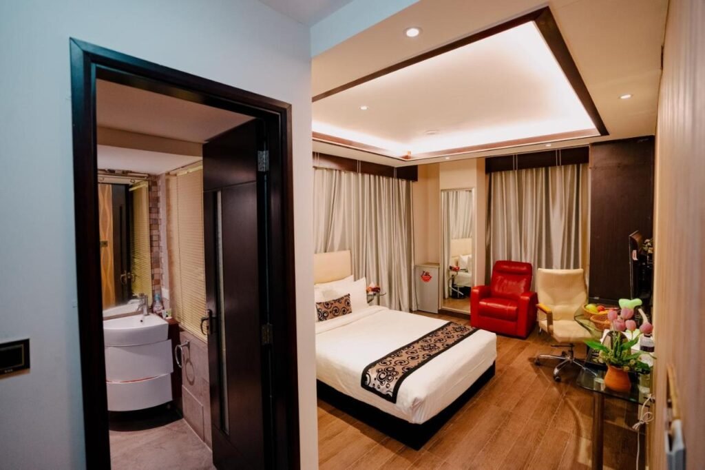 Deluxe room with king bed, red recliner and en-suite bathroom at Royal Residence Dhaka, Baridhara